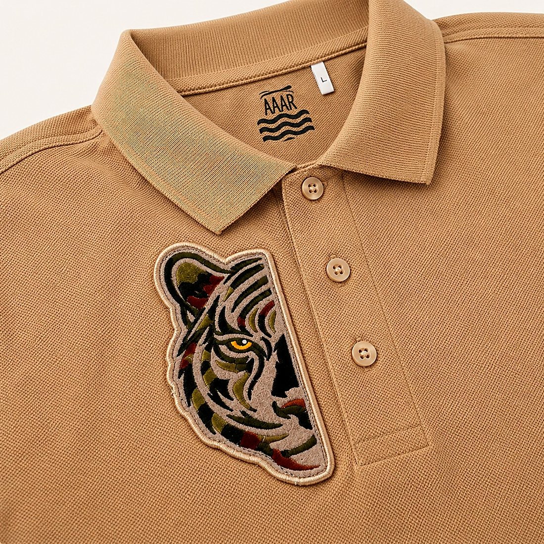 Close detail of the embroidered green half tiger on the Safari Polo in Sand